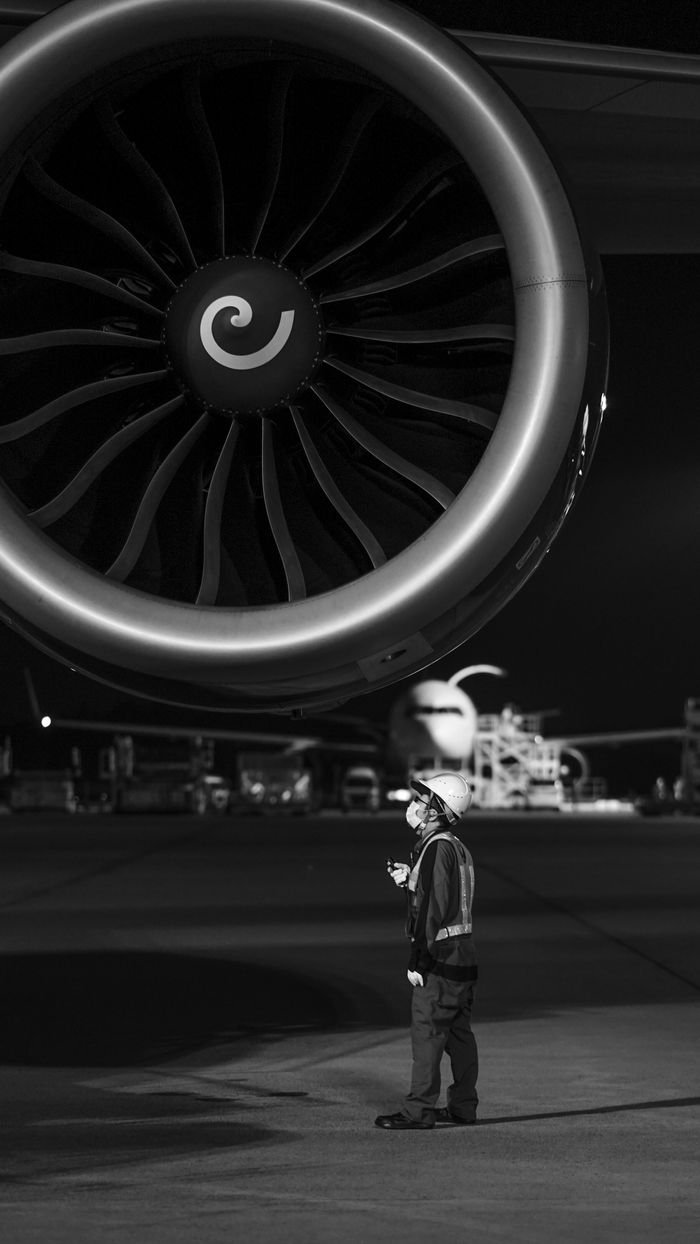 Black and white image of a maintenance technician inspecting an airplane engine at night.